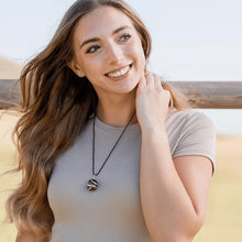 Load image into Gallery viewer, Outdoor lifestyle shot of a woman wearing a polished black onyx pendant on a black cord necklace.