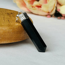 Load image into Gallery viewer, Black onyx stone jewelry pendant showcased with a yellow prop stone on a smooth white studio background.