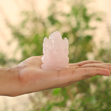 Load image into Gallery viewer, Clear Quartz Ganesh crystal figurine held in hand against a natural background of trees and foliage
