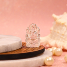Load image into Gallery viewer, Clear quartz Ganesh figurine displayed on round marble and wooden platforms with pearls and a shell in soft pink background