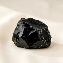 Load image into Gallery viewer, Black Obsidian Raw Stone displayed fully on white silk cloth to show its natural colour, shape and finish