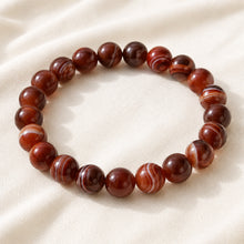 Load image into Gallery viewer, Red Sulemani Hakik Bracelet displayed fully on white silk cloth to show its natural colour, shape and finish