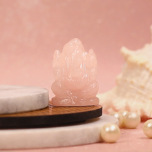 Load image into Gallery viewer, Rose Quartz Ganesh crystal figurine placed on round marble and wooden platforms, with pearls and seashell in pink background