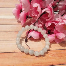Load image into Gallery viewer, White bead bracelet on a wooden table with pink flowers beside it