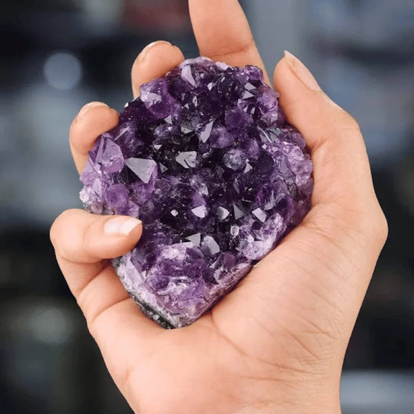 Amethyst raw stone cluster held on hand, symbolizing calm, insight, and protection.