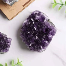 Load image into Gallery viewer, Amethyst raw stone cluster placed on a white table, symbolizing calm, insight, and protection.
