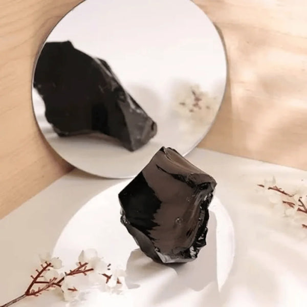 Black Obsidian raw stones placed in front of a mirror, showing their reflection, symbolize protection, grounding, and truth.
