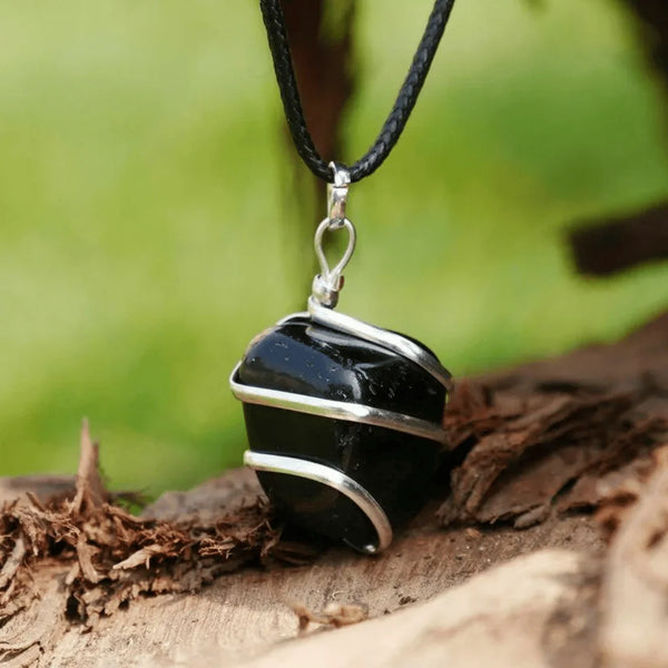 Natural black obsidian crystal pendant wrapped in silver wire and displayed on a wooden surface.