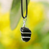 lack onyx pendant wrapped in silver wire hanging outdoors against a blurred nature background.