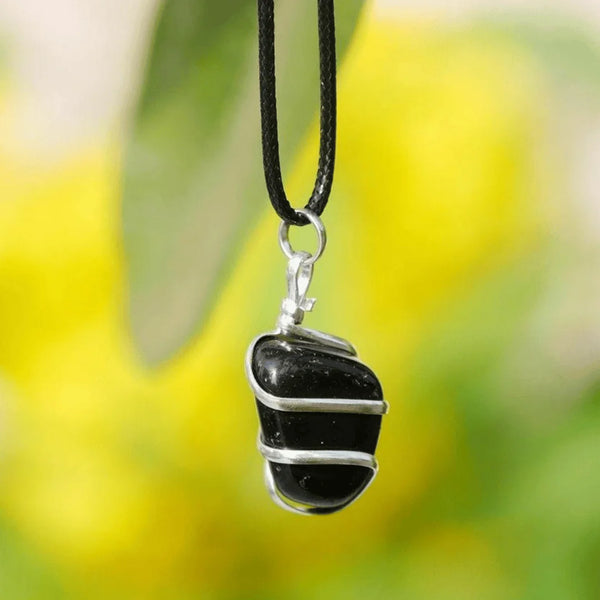 lack onyx pendant wrapped in silver wire hanging outdoors against a blurred nature background.