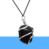 Handmade black onyx crystal pendant wrapped in silver wire, displayed on wood outdoors.