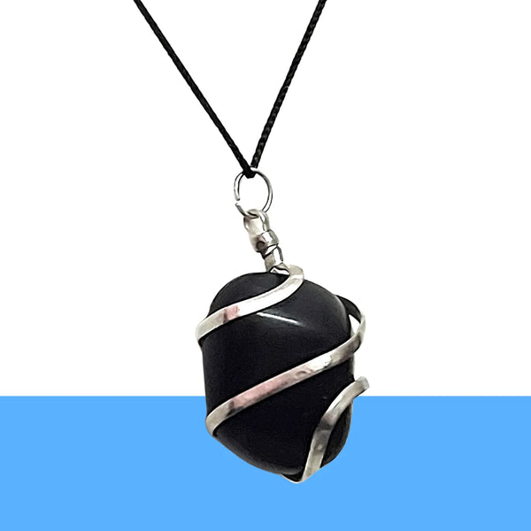 Handmade black onyx crystal pendant wrapped in silver wire, displayed on wood outdoors.