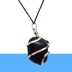 Handmade black onyx crystal pendant wrapped in silver wire, displayed on wood outdoors.