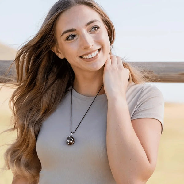 Outdoor lifestyle shot of a woman wearing a polished black onyx pendant on a black cord necklace.