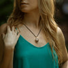 A woman wearing a black onyx crystal pendant wrapped in silver wire on a black cord necklace outdoors.