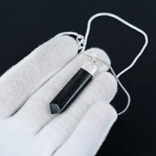 Load image into Gallery viewer, Black Tourmaline pencil-cut pendant resting on an open hand, captured in a sharp close-up with soft natural lighting.
