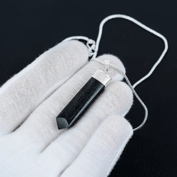 Black Tourmaline pencil-cut pendant resting on an open hand, captured in a sharp close-up with soft natural lighting.