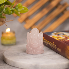 Load image into Gallery viewer, Clear quartz Ganesh figurine displayed with a Bhagavad Gita book and a lit candle on a plain background
