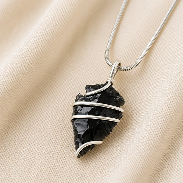 Black Obsidian Arrowhead Pendant displayed fully on white silk cloth to show its natural colour, shape and finish