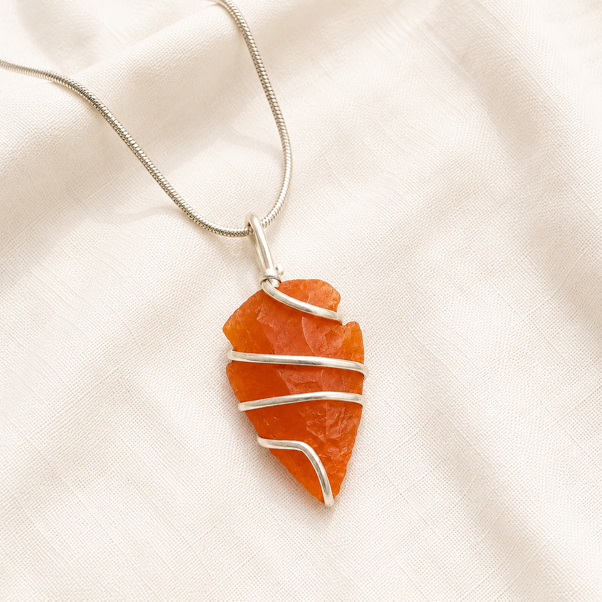 Carnelian Arrowhead Pendant displayed fully on white silk cloth to show its natural colour, shape and finish