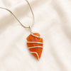 Carnelian Arrowhead Pendant displayed fully on white silk cloth to show its natural colour, shape and finish