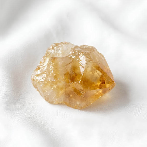 Citrine Raw Stone displayed fully on white silk cloth to show its natural colour, shape and finish