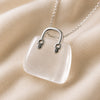 Clear Quartz Mini Handbag Pendant displayed fully on white silk cloth to show its natural colour, shape and finish