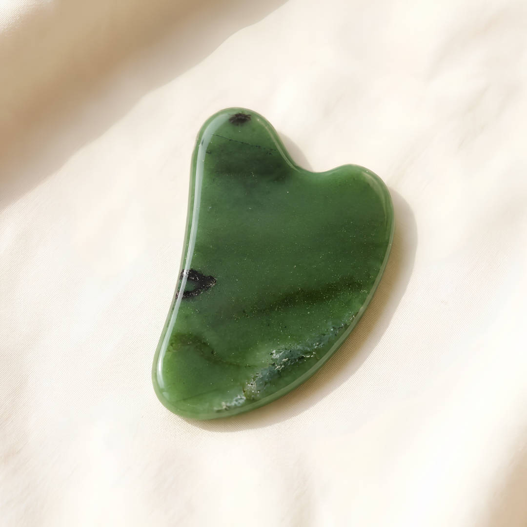 Green Jade Gua Sha displayed fully on white silk cloth to show its natural colour, shape and finish