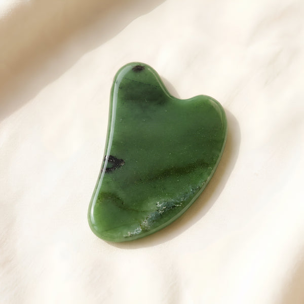 Green Jade Gua Sha displayed fully on white silk cloth to show its natural colour, shape and finish
