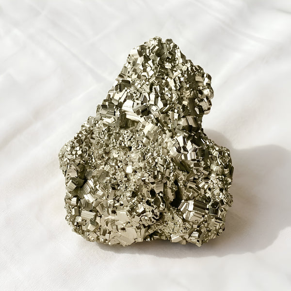 Pyrite Raw Stone displayed fully on white silk cloth to show its natural colour, shape and finish