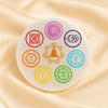 Seven Chakra Selenite Round Charging Plate displayed fully on white silk cloth to show its natural colour, shape and finish