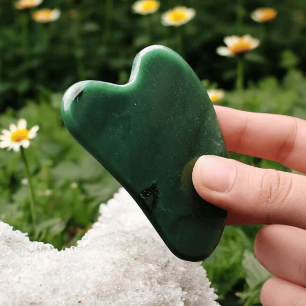 Green Jade Gua Sha face crystal held in hand, promoting cooling, skin renewal, and prosperity benefits.