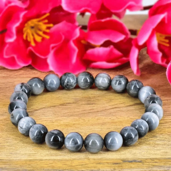 Natural grey crystal bracelet on a wooden table with pink flowers in the background.