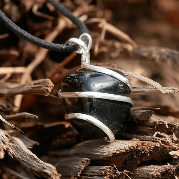 Black onyx pendant wrapped in silver wire hanging outdoors against a blurred nature background.
