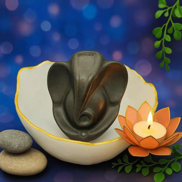Lord Ganesha decorative showpiece placed in a white bowl with a lotus candle and smooth stones for spiritual home décor.