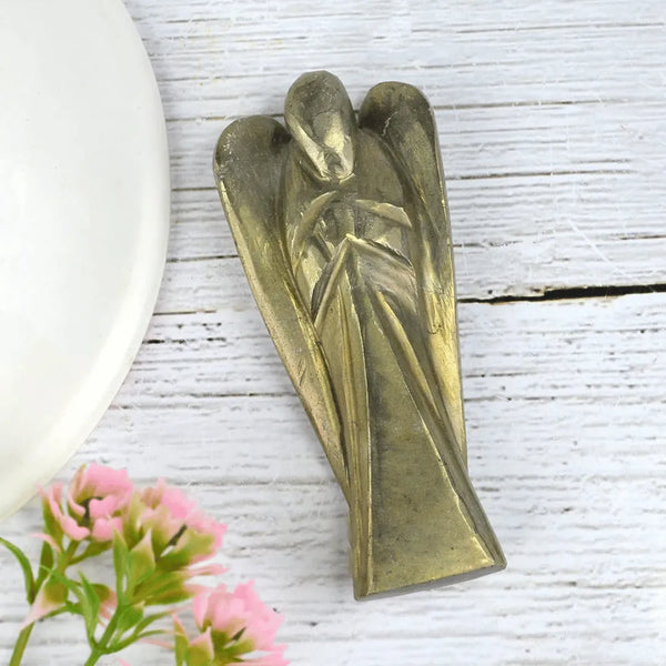 Pyrite angel figurine on a white wooden surface with pink flowers
