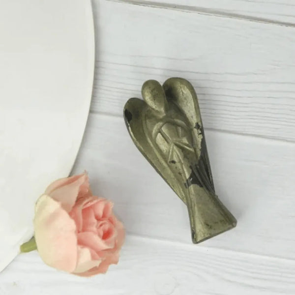 Pyrite angel figurine placed on a white wooden surface beside a soft pink rose