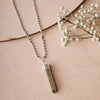Pyrite point pendant with silver cap and chain displayed on a soft pink background.