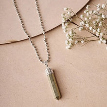 Load image into Gallery viewer, Pyrite point pendant with silver cap and chain displayed on a soft pink background.
