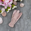 Rose Quartz Angel figurine placed on grey surface with natural stones and white flowers around.