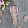 Rose Quartz Angel figurine lying on a grey surface with rose quartz stones and white flowers.