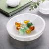 Spiritual cleansing crystals arranged in a selenite bowl next to a book and green plant leaves