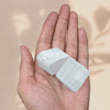 Selenite raw crystal cluster resting on the palm against a soft pink background, symbolizing cleansing and clarity.