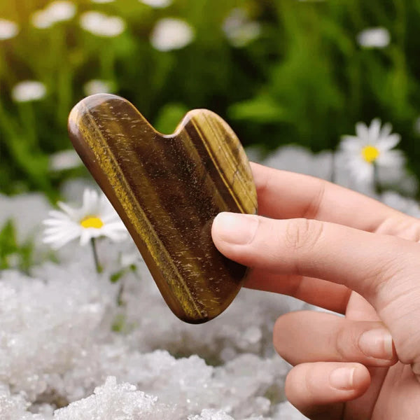 Tiger Eye Gua Sha face crystal held in hand, used for energizing massage, willpower and facial balance.