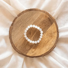 Load image into Gallery viewer, White bead bracelet placed on a round wooden table.
