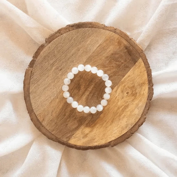White bead bracelet placed on a round wooden table.
