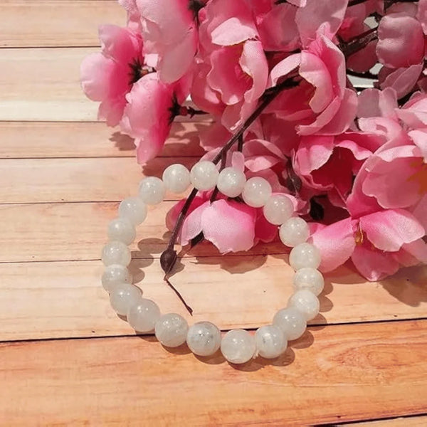White bead bracelet on a wooden table with pink flowers beside it